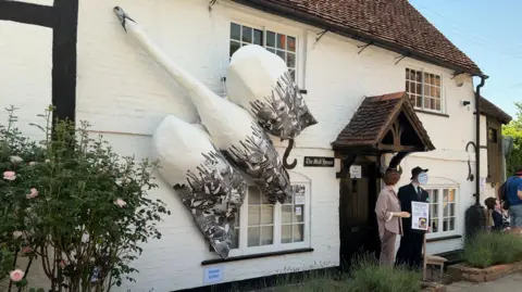 A huge white and grey swan scarecrow sits on the white wall at the front of a house.