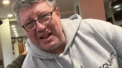 Stephen is wearing a grey hoodie and glasses. 