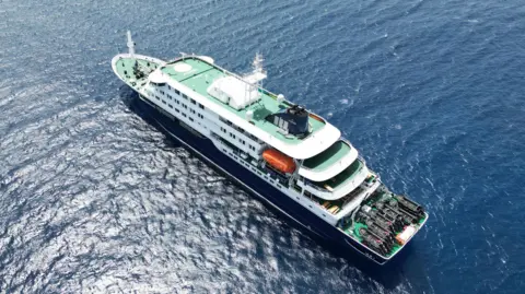 Getty Images An aerial view of the MV Hondius which is a cruise ship with a blue and white livery. It is seen in the open ocean on a calm day and the sea is a dark blue