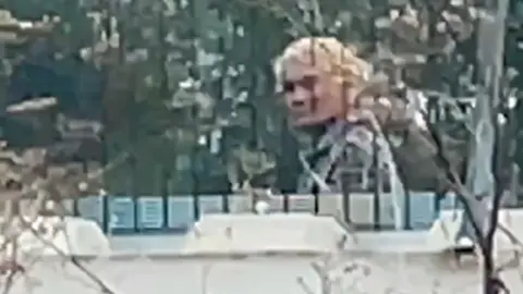 BBC A zoomed in image from our undercover footage of a Vietnamese people smuggler, hair dyed blond, walking behind a fence