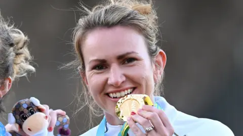 Getty Images A woman with dark hair tied up in a bun smiling at the camera. She is holding up a gold Commonwealth Games medal to her mouth.