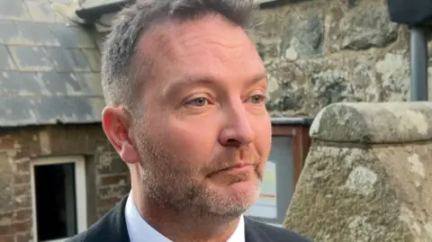 BBC John Guille in blue suit and red tie