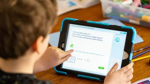 PA Media Wilfred, aged 7, does maths activities on an iPad as he takes part in home schooling