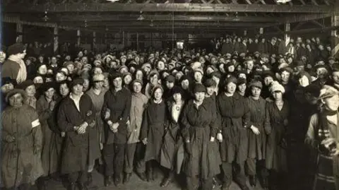 Leeds City Council A black and white photograph of hundred of women in a factor standing looking towards the camera.