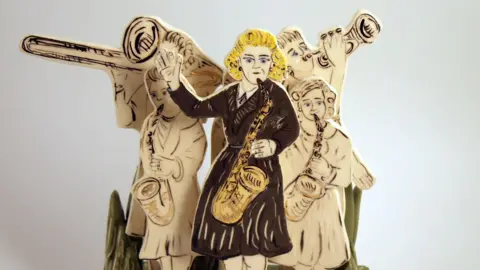 Leeds City Council A hand-drawn, white statue of a band. At the front is a woman with blonde hair wearing a black dress holding a saxophone.