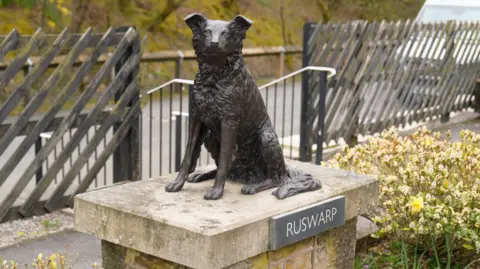 Nick Wooley/BBC A grey-bronze statue of a border collie sat on a stone plinth