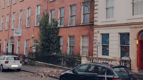 PSNI Shows several red-bricked Georgian buildings on a street with two cars