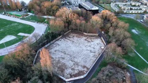 Peterborough from Above A drone image taken form above of a brown field covered with a snow dusting with fencing around it. It is surrounded by trees and greenery around it.