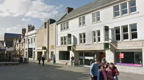 Google Exterior picture of Queensgate - white building with rectangle windows and a big yellow M on the wall for McDonald's and people walking in front of it
