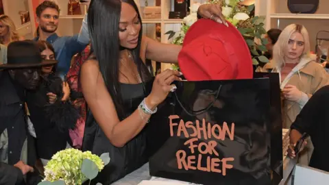 Getty Images Naomi Campbell putting a red hat into a Fashion for Relief bag