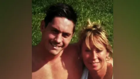 Family handout Jamie Attwood with short dark hair smiling at the camera with his arm around his mother, who has medium-length brown hair and is wearing a white top.  They are outside standing on grass.