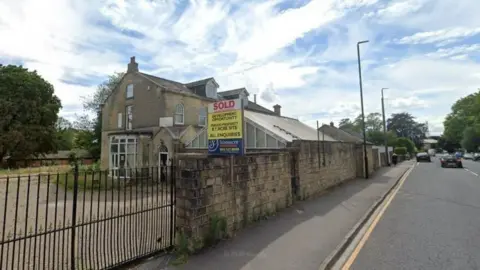The building with a gate and brick wall around it as well as a sign saying "sold".