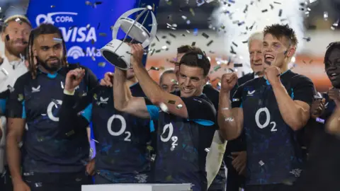 George Ford lifts a trophy as ticker tape falls around him and his team-mates