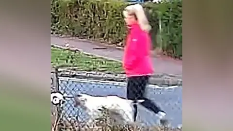 Suffolk Police Anita Rose in a pink zip-up coat, walking a dog. The image is blurred.