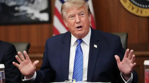 Trump at Camp David in blue jacket and blue tie holding both hands up 