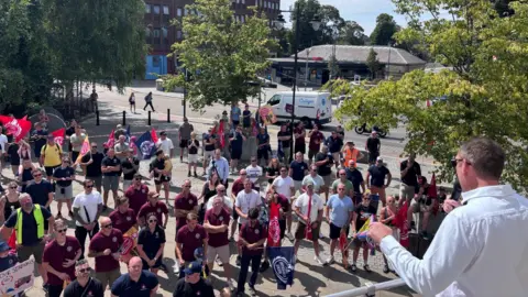 A man in white shirt is doing a speech during a rally outside a town hall.