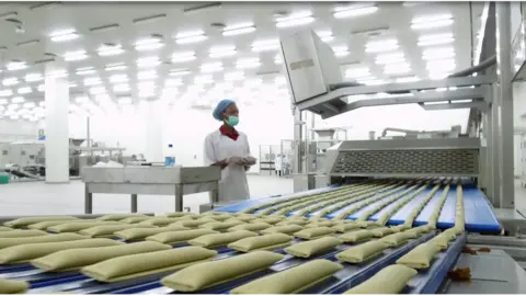 A woman monitoring a machine making sausage rolls in a factory