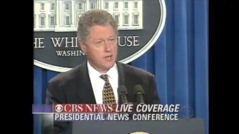 An old image of Bill Clinton standing at a podium at the White House.
