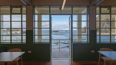 James Kerr An open air pool can be seen, taken from inside a restored pavilion building.