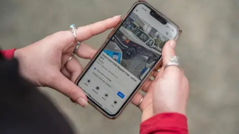 Getty Images Person holds phone with Facebook Marketplace open, showing a car.