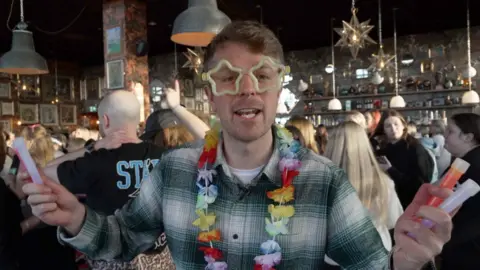 A man in a flower garland holds slow sticks