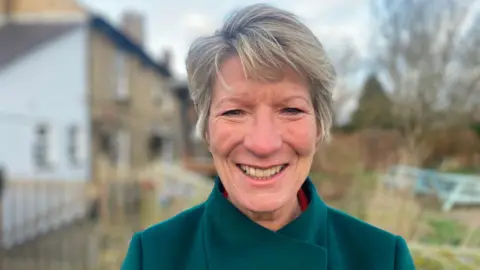 Jenny Kirk/BBC Pippa Heylings, the Liberal Democrat MP for South Cambridgeshire, is smiling at the camera. She has short, fair hair and is wearing a blue coat