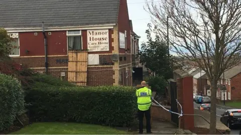 A policeman standing at the side of Manor House. Police tape covers the entrance.