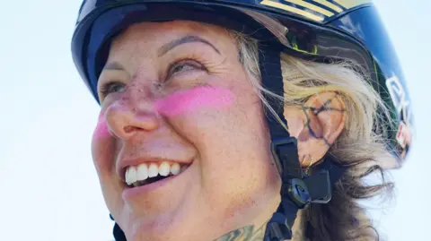 PA Media A woman wearing a cyclist helmet looking up and smiling