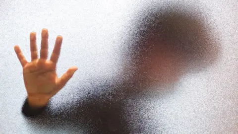 Getty Images Blurred boy holds hand against glass door