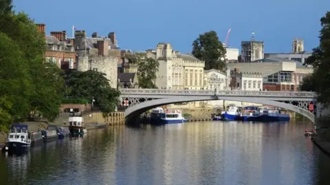 Lendal Bridge in York on a sunny day, photographed from Scarborough Bridge. Boats are on the river.