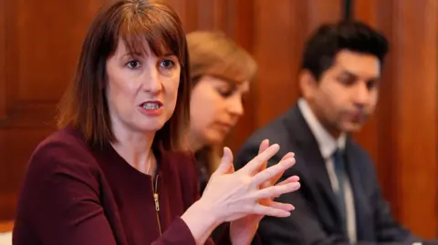 PA Media Rachel reeves with her hands clasped together wearing a maroon top