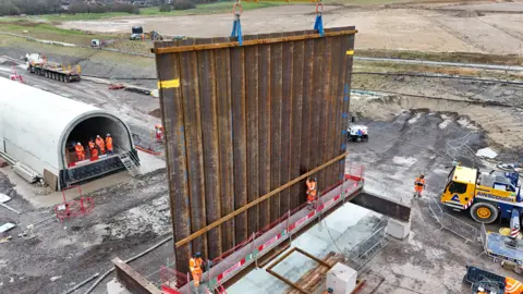 A large steel wall in the middle of a reservoir construction site 
