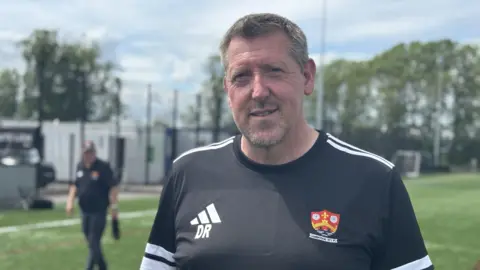 Zoie O'Brien/BBC A head and shoulders image of a man wearing a black and white top. He is standing on a football pitch and looking into the camera.