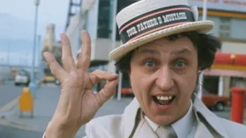 Sir Ken Dodd with straw boater on Blackpool prom with the tower in the background.