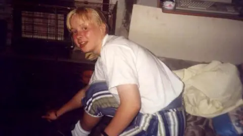 Faded photo of a teenage girl sitting on a sofa in a living room, with a gas fire in the background.