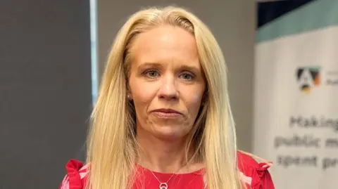 A woman with long blond hair, looking at the camera. She has a red top on.