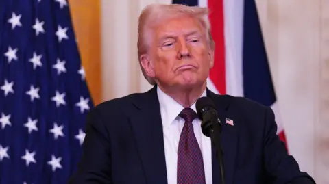 The media Donald Trump in front of the American flags and the United Kingdom, wears a dark suit, a white shirt and a tie in red and blue