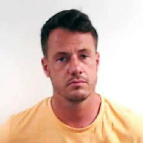 Police Scotland A mugshot of Cameron Ross, looking straight at the camera wearing a yellow T-shirt against a white background.