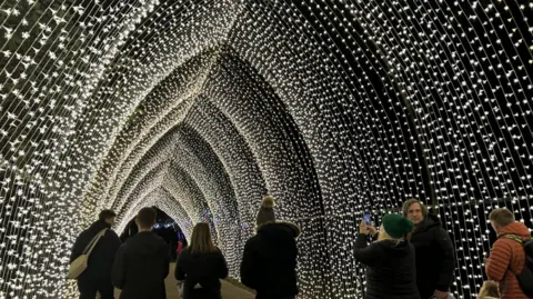 People walking at night time through a tunnel made of walls of tiny fairy lights 