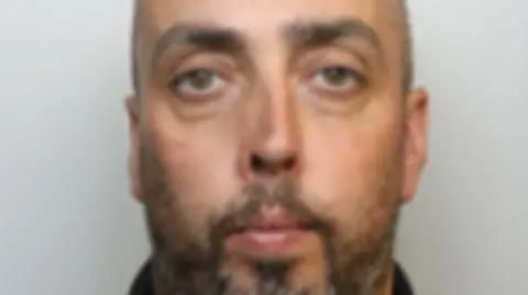 Avon and Somerset Police A close-up custody photos of a man with greying hair, a beard and green eyes
