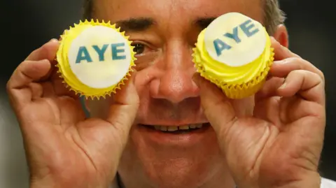 PA Media Alex Salmond poses with two Aye cupcakes