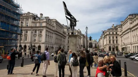Getty Images Crowd gathers around a statue in central London, with historic buildings lining the street