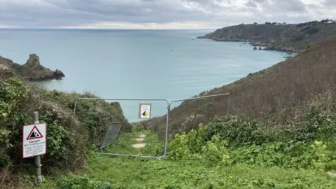 BBC A photo of the steps leading to a beach on Guernsey's coast. The steps have been closed off with metal fencing. The sea is in the background.