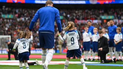 Getty Images Harry Kane of England walks out with their children, Ivy Jane Kane and Vivienne Jane Kane prior to the UEFA EURO 2024 qualifying round group C match between England and Ukraine at Wembley Stadium on March 26, 2023 in London, England.