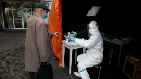 Reuters A health worker in protective suit gives a document to man, amid the coronavirus disease (COVID-19) outbreak, at a test centre in front of a hospital in Warsaw, Poland on 27 October 2020.