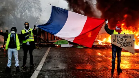 AFP Protesters hold a French flag near a burning barricade in Paris during a protest of yellow vests