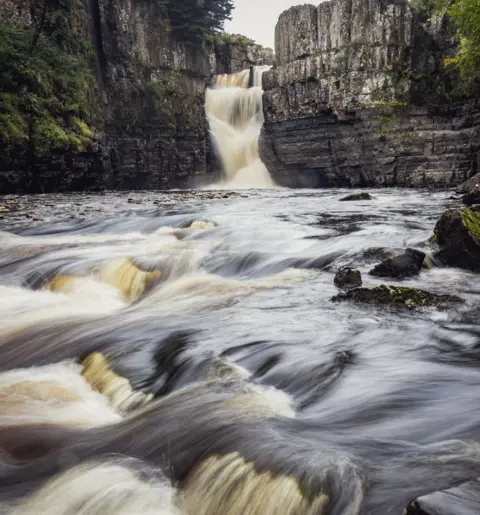 @eoinfkellyphotography Water rushing over rocks with a waterfall in the background