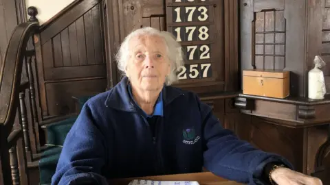 JOHN DEVINE/BBC Evelyn Hamps, dressed in a navy blue fleece, sitting inside Doddington Methodist Church