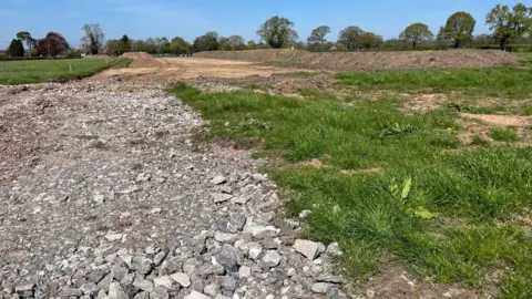 There are large mounds of dirt on the right-hand side of the filed and and rubble on the left.