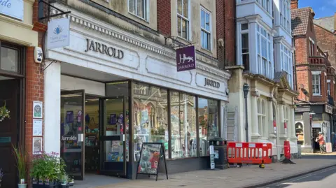 BBC Line of shops showing the facade of the Jarrolds book store in Cromer, with an A board outside and some road work barriers further along